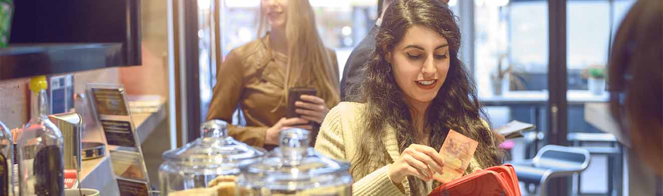 Junge Frau bezahlt eine Rechnung an der Kasse eines Bistros in bar