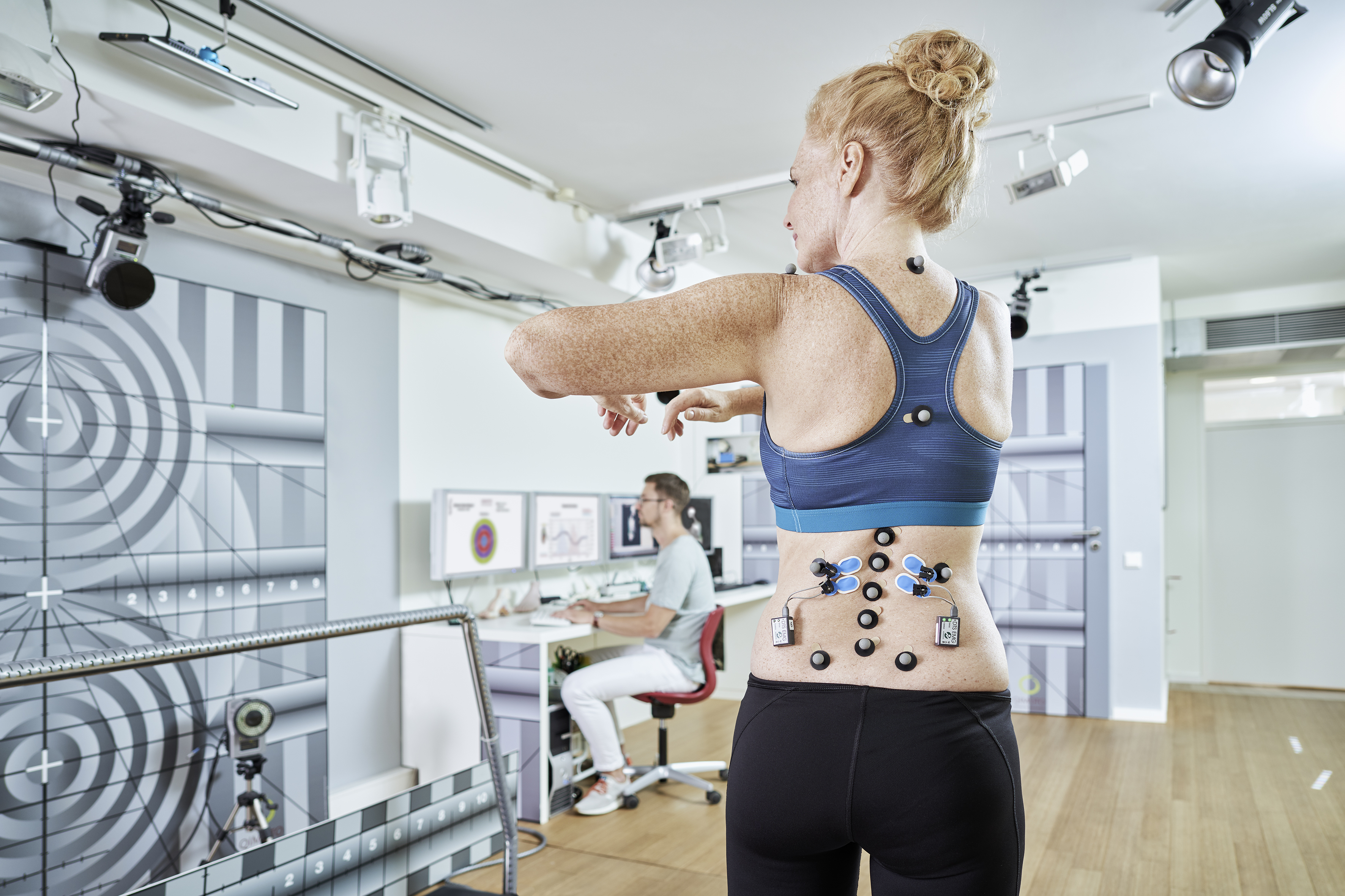 Frau mit Sensoren auf Rücken bei Bewegungstest, Orthopäde analysiert Daten am Computer im Labor. 