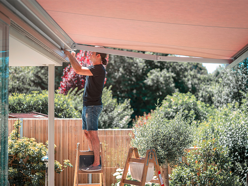 Handwerker stellt eine Markise mit Inbusschlüssel ein und überprüft die Mechanik auf der Terrasse.