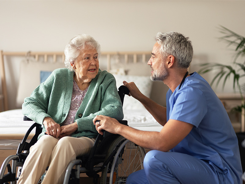 Pflegepersonal führt regelmäßige Gesundheitskontrolle bei älterer Frau in ihrem Zimmer durch, einfühlsame und professionelle Betreuung.