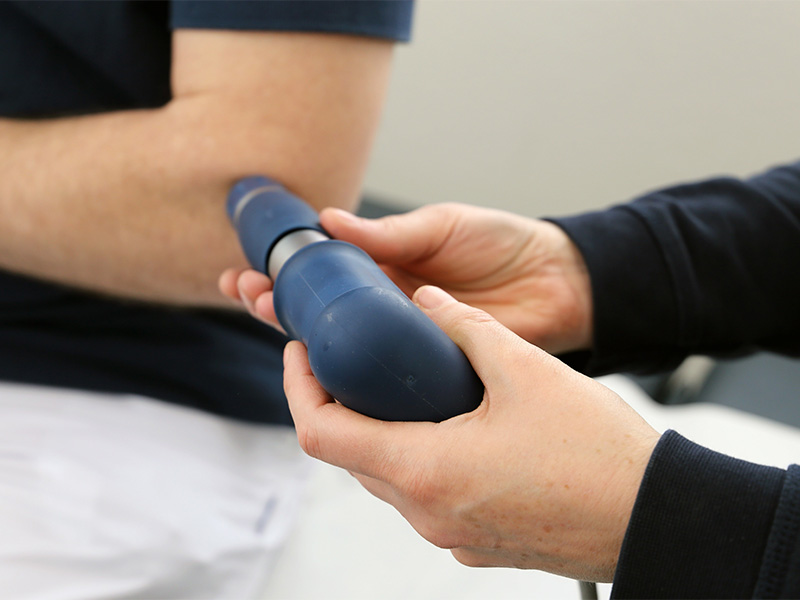 Stoßwellentherapie in Wiesbaden wird am Ellenbogen eines Patienten durch eine medizinische Fachperson durchgeführt.